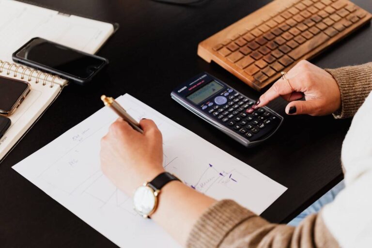 Mastering the Basics: Finance Essentials Every UK Small Business Needs The finance essentials. A photo of a person's hands, sat at a desk using a calculator and writing on a piece of paper.