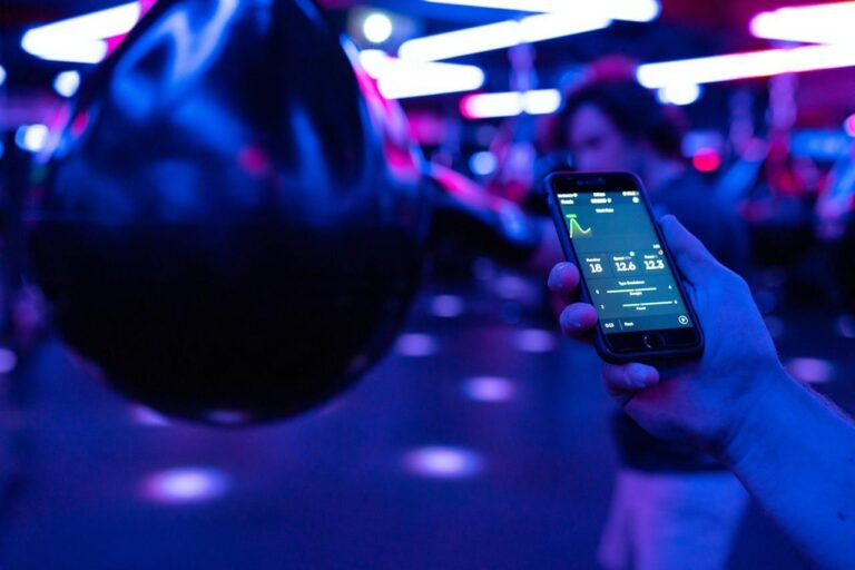 AI-Powered Personal Training: How Smart Coaching is Changing Fitness in 2025 AI-powered personal training.A photo of someone hitting a punch bag in the background, and a phone & hand in focus in the photo displaying a fitness tracking AI app.